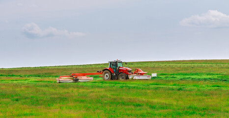 A red tractor mows the grass on a farmer's field. Two mowers will mow a large area of the field.