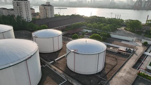 Oil storage tanks in rows along the riverside. Drone aerial view. Oil storage tanks in the sunset time, flying over the tanks along the river.  Industry, business, economy concept b-roll footage.