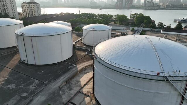 Oil storage tanks in rows along the riverside. Drone aerial view. Oil storage tanks in the sunset time, flying over the tanks along the river.  Industry, business, economy concept b-roll footage.