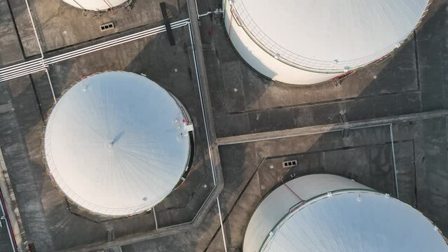 Oil storage tanks in rows in the factory. Drone aerial view. Oil storage tanks in the sunset time with light in the side, flying over the tanks.  Industry, business, economy concept b-roll footage.