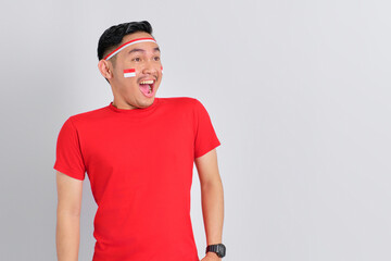 Shocked young Asian man celebrating Indonesian independence day looking at copy space with open mouth isolated on white background