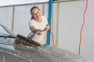 A young woman washing a car smiles. A girl in a white T-shirt with blond hair braided in a ponytail...