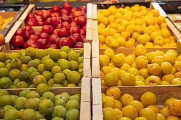 close-up fresh fruit in a store in wooden boxes. Fresh plums yellow, red and green on the counter in a store in wooden boxes.