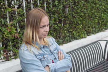 Obraz premium a girl of European appearance with blond hair in a red dress, a denim jacket sits on a bench offended. Human emotions