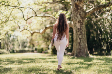 back view of a beautiful woman in a white tracksuit walking in the park with a laptop