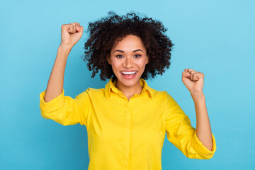 Photo of hooray curly hairdo young lady hands fists wear yellow blouse isolated on blue color background