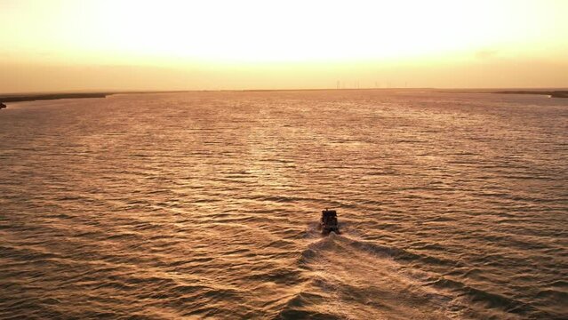 Speed boat silhouette cruise during sunset, golden light reflections on water,  Aerial descending