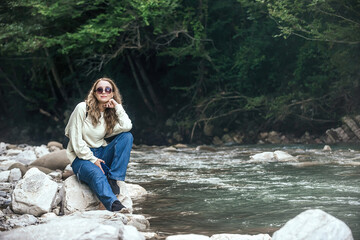 portrait of a beautiful traveler girl with long wavy hair against the backdrop of a green forest and a mountain river
