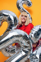 Fototapeta na wymiar a bright vertical photo on a yellow background of a happy, smiling woman, turning her face to the side with balloons in the form of silver numbers
