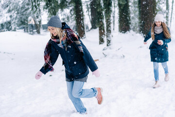 Fototapeta na wymiar Two female girlfriends play snowballs in the park during a snowfall