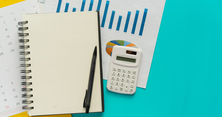 close up top view on blank book with pen and calendar and statistics report on teal background for...