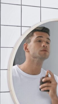 vertical video of man in white t-shirt spraying perfume and looking at mirror
