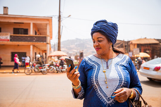 An African woman uses her smartphone while she is in the city center, she wears traditional african clothes.