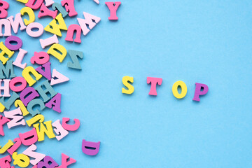 Stop. inscription from colored wooden letters. Light blue paper background. Copy space, top view.