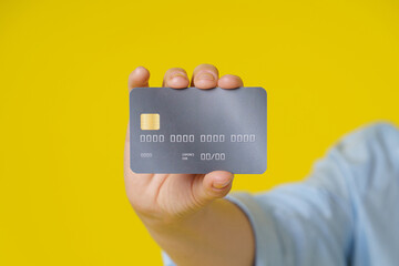 Credit, debit cad close up in hand of mature woman showing it on camera, online payment or shopping online, isolated on yellow background. E-commerce, online banking concept