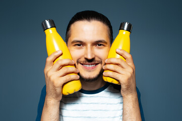 Studio portrait of young joyful man, holding two yellow eco bottles close to his face.