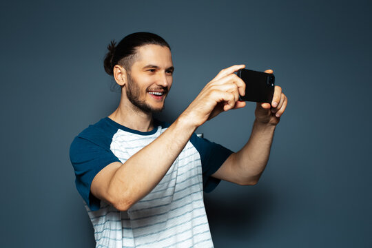 Studio portrait of young joyful man, taking photos with smartphone.