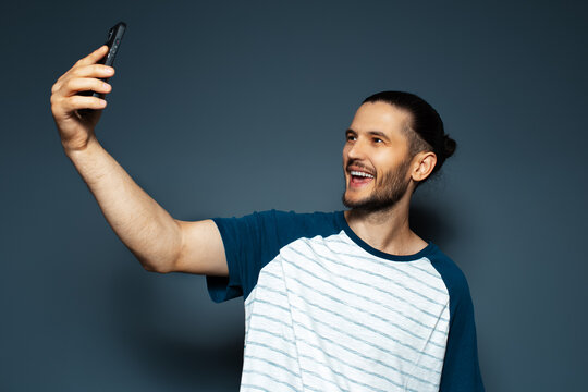 Studio portrait of young handsome smiling guy, taking selfie with smartphone.