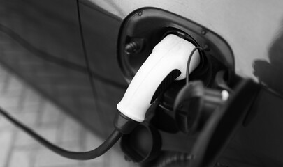 Plug-in hybrid EV car charging at charge station, home. Black and white photo. Close-up view.