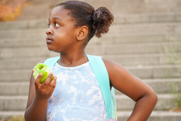 Elementary girl with backpack eating apple at the school entrance. healthy eating for children...