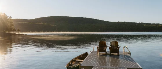 Cercles muraux Canada Panoramic view of the idyllic lake in Canada with a small boat and chairs on the shore