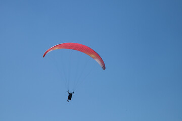 Parapente rouge dans un ciel bleu : préparation à l'atterrissage