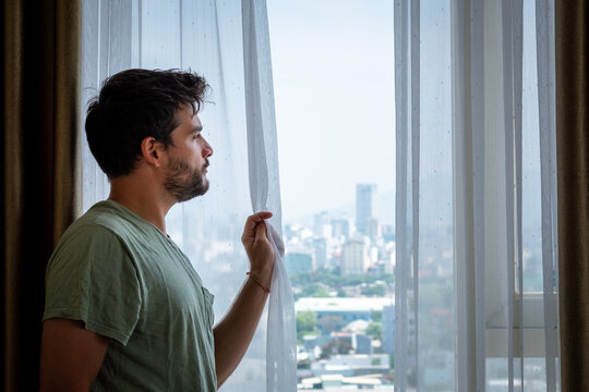 Hombre mirando por la ventana de su habitaci&oacute;n perdido en sus pensamientos. 