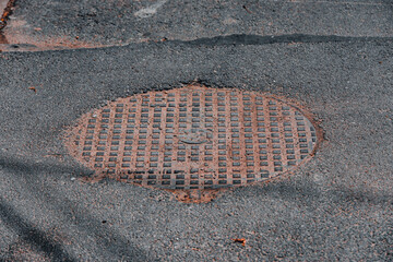 Round metallic sewer cap or manhole cover with rust on the street with asphalt