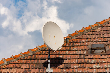 Satellite dish antenna on a tiled roof of an old home for signal receiving