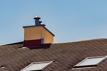 Tiled roof of a home with chimney and attic windows on a clear blue sky