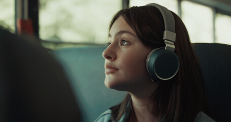 Girl teenager traveling bus with headphones close up. Brunette listening music.
