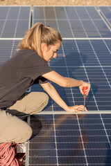 Top view of young woman screwing a screw to assamble the photovoltaic solar panels on the roof of a...