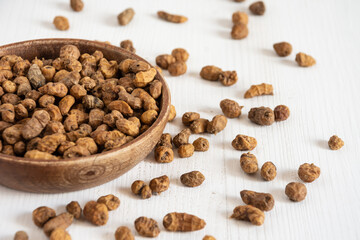 Close-up of wooden bowl with tiger nuts on white table, selective focus, horizontal