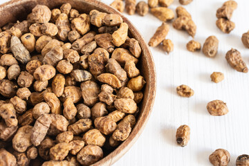 Aerial view of wooden bowl with tiger nuts on white table, selective focus, white background, horizontal