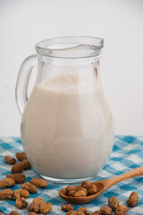 Top view of glass pitcher with horchata and tiger nuts on blue cloth, selective focus, white background, vertical