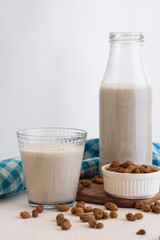 View of bottle and glass with horchata and tiger nuts on blue cloth, selective focus, white...