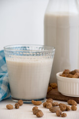 Close-up of bottle and glass with horchata and tiger nuts on white table, selective focus, white background, vertical