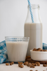 View of bottle with blue straw and glass with horchata and tiger nuts on white table, selective focus, white background, vertical
