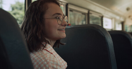 Smiling teen girl sitting school bus talking with friends. Student chatting.