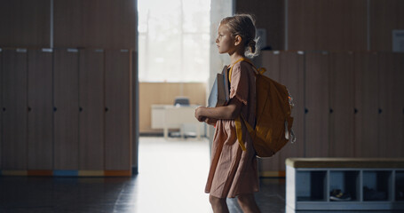 Schoolgirl walking holding books in empty hall alone. Pupil passing classrooms.