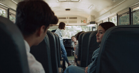 High school students sitting communicating in schoolbus. Pupils waving friend.