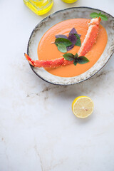Bowl of bisque with crab and fresh basil on a light-beige marble background, vertical shot with space, flat lay