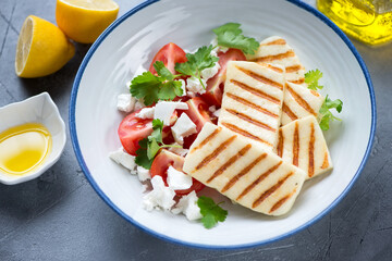 Plate with slices of grilled haloumi cheese, tomato wedges and feta, middle close-up, selective focus