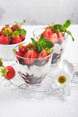 Trifles. Brownies, fresh strawberry and mascarpone cream servered in layers on glass on white background. Portion desserts. No baked brownie cheesecake with fresh berries in a glass.