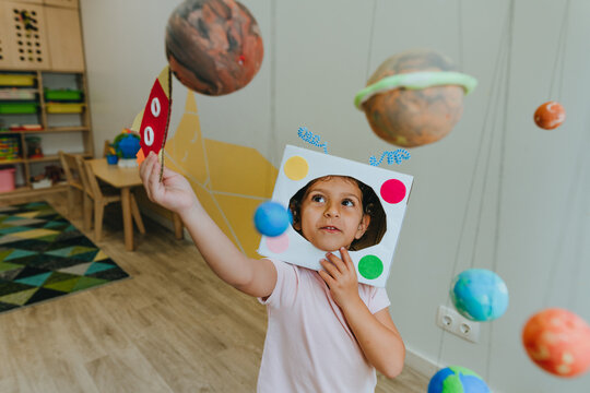Little girl playing with paper spaceship learning Solar system planets