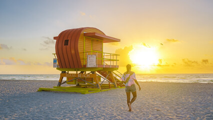South Beach Miami Florida, beach hut lifeguard hut during sunset. beautiful sunset on Miami Beach. Young men walking on the beach during sunset - obrazy, fototapety, plakaty