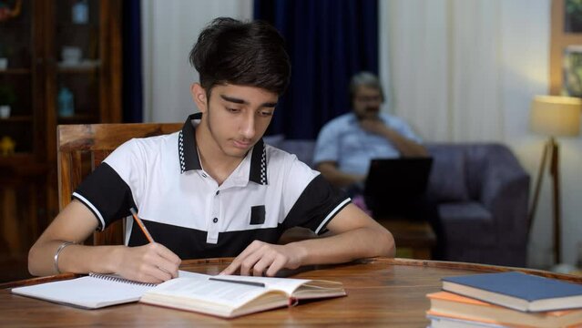 A handsome teenage boy posing for the camera while making study notes - school student  preparing for competitive exams . A young boy studying at home - studious child  exam preparations  late nigh...