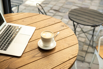Laptop and a cup of coffee on a table in a street cafe. Remote work concept