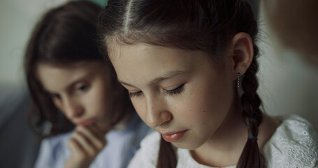 Two schoolgirls sitting together at break close up. Preteen girls looking down.