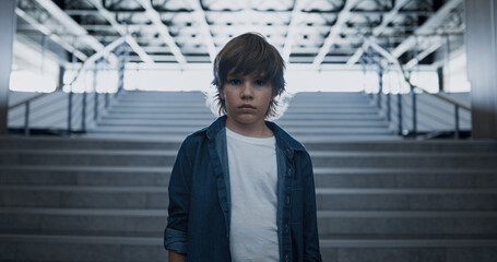 Depressed school boy standing alone at empty staircase close up. Fearful eyes
